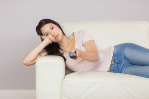 Bored asian girl lying on the couch watching tv at home in the sitting room